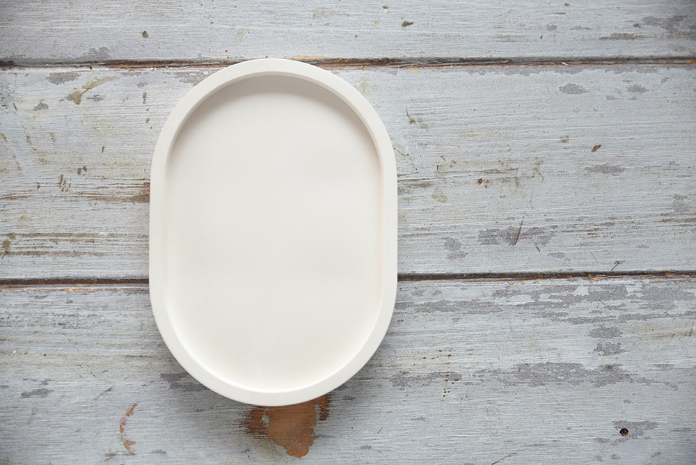 Ovális gipsz tálca - Modern asztali rendező Beltéri gipsz kiegészítő: egy kisméretű, ovális alakú, matt tálca peremmel. A minimalista design tökéletessé teszi ékszertartónak vagy kulcsok tárolására, vagy dekorációnak, rusztikus fa felületen fotózva.