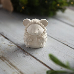 Közeli fotó egy részletgazdag, kötött mintás ruhát viselő gipsz egérkéről rusztikus fa asztalon.