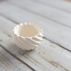 Közeli fotó egy különleges, csavart és hullámos falú gipsz mécsestartóról (Fénygömb) rusztikus szürke fa felületen.