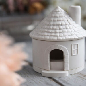 Beltéri gipsz dekoráció: egy minimalista, fehér gipszből készült házikó alakú füstölőtartó apró ablakokkal és kéménnyel. A termék egy rusztikus fa felületen látható, letisztult skandináv design elemekkel.