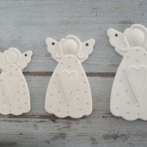 Három különböző magasságú, letisztult stílusú dekor gipsz angyalka figura szív motívummal, rusztikus szürke fa háttéren elrendezve.