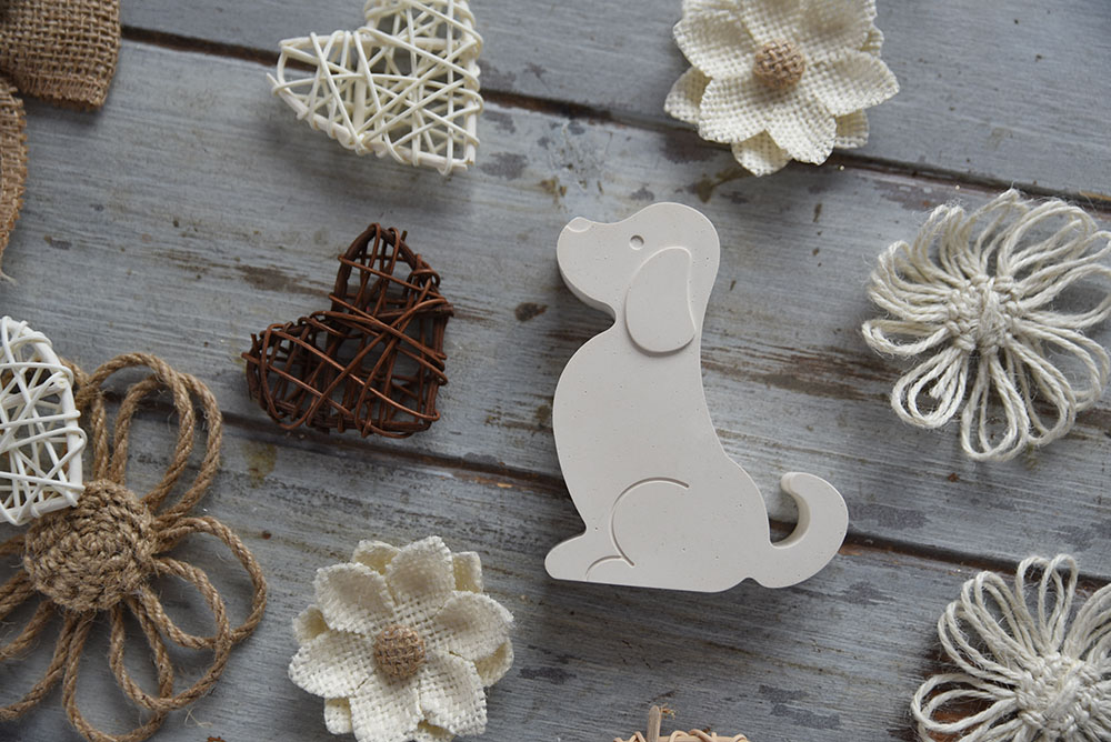 kezmuves-dekor-gipsz-beagle-kutya-figura-ajandek Profilból fotózott minimalista fehér gipsz beagle kutya figura rusztikus fa háttéren, juta virágokkal és fonott szívekkel körülvéve.