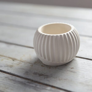 Beltéri gipsz dekoráció: egy gömbölyű, fehér MiraStone mécsestartó függőleges bordázott mintával. A termék egy rusztikus szürke fa asztalon látható, a háttérben egy dekoratív fadobozzal, amely a természetes lakberendezési stílust hangsúlyozza.