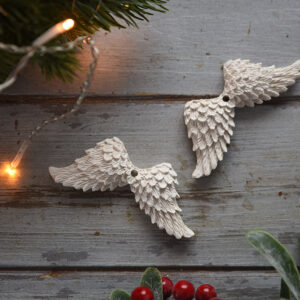 Felülnézeti kép egy pár aprólékosan kidolgozott gipsz angyalszárnyról, piros bogyós ággal és meleg fényű ünnepi izzókkal dekorálva.